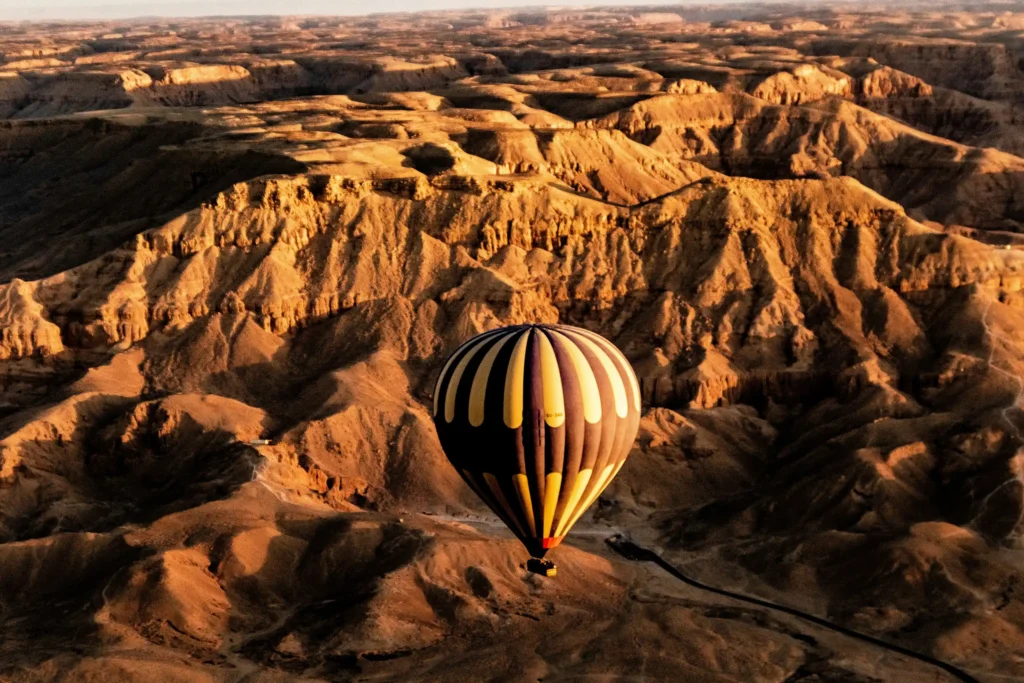Montgolfière survolant les ravines érodées de la montagne thébaine en lumière rasante au lever du soleil