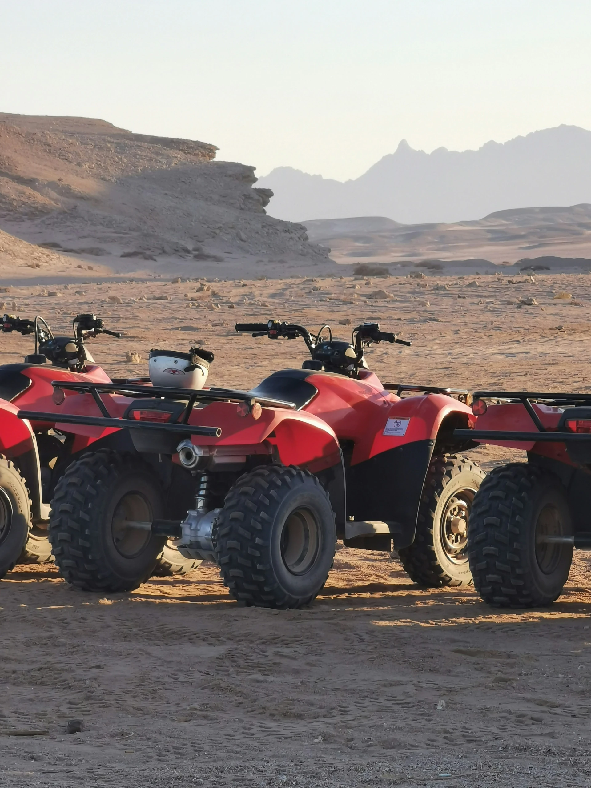 Quads rouges à l'arrêt dans le désert, casques posés sur les porte-bagages, montagnes découpées à l'horizon